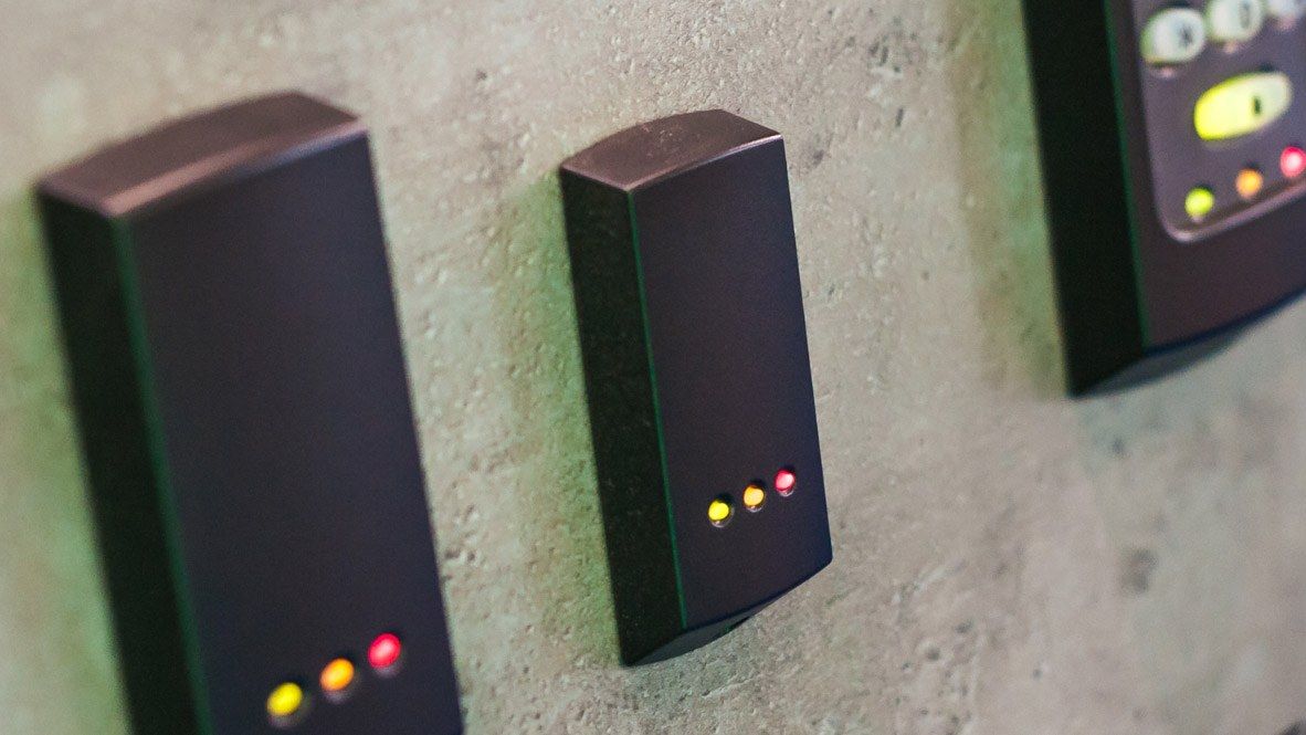 Access control readers and a keypad with yellow, orange and red status lights, mounted on a concrete wall