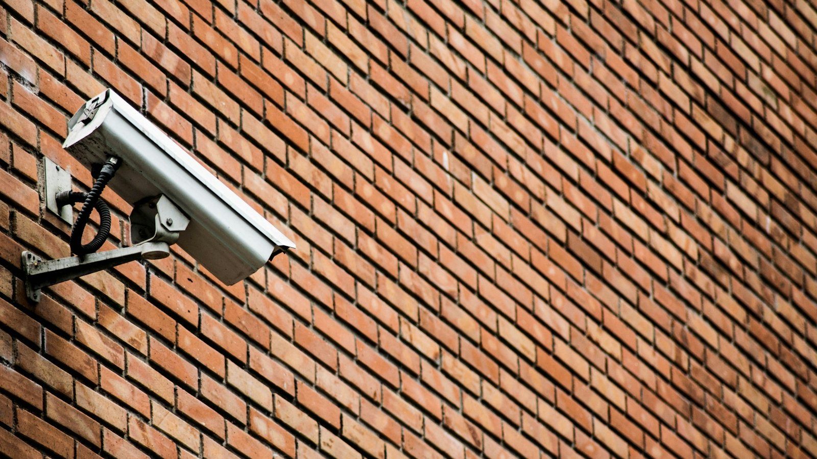 A white bullet CCTV camera on a bracket fixed to a brick wall