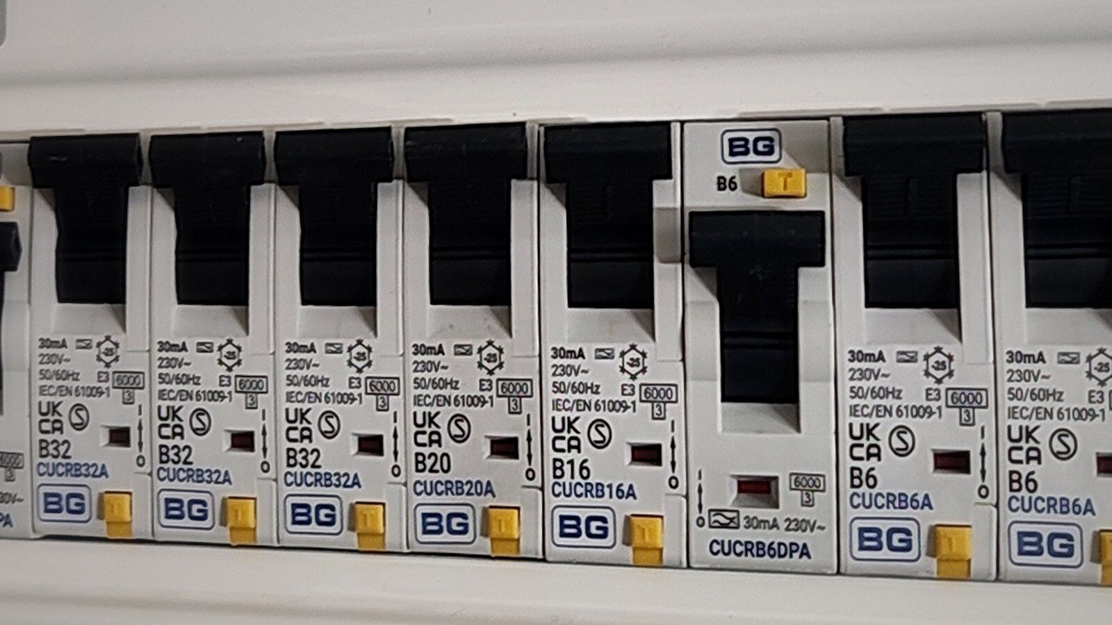 A close-up of 30 mA RCBOs in a modern BG consumer unit, seen at an angle, all switched on