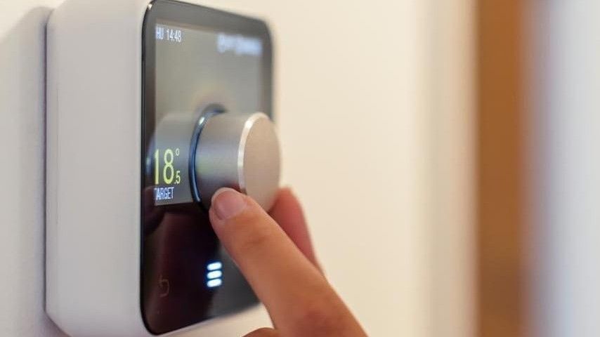 A finger turning the dial of a smart thermostat on a wall