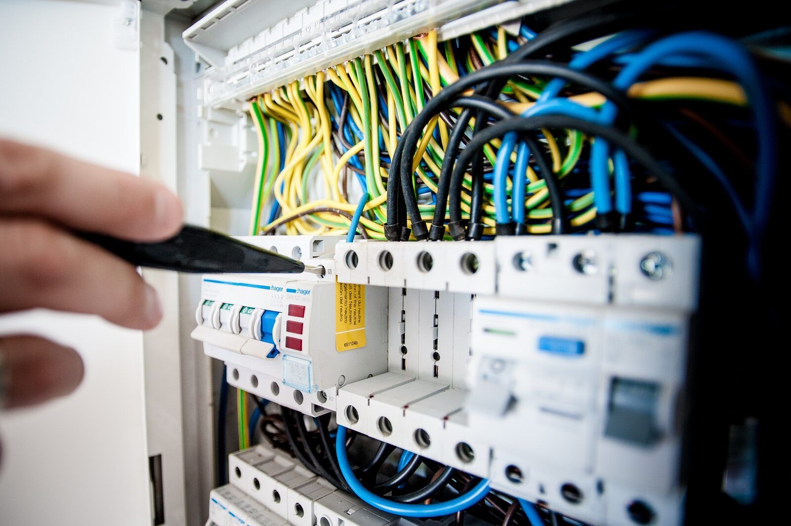 Hand with a screwdriver at a consumer unit with RCDs, circuit breakers and neatly dressed cables