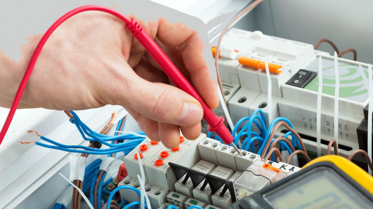 Hand holding a red test probe on a terminal, with a multimeter alongside