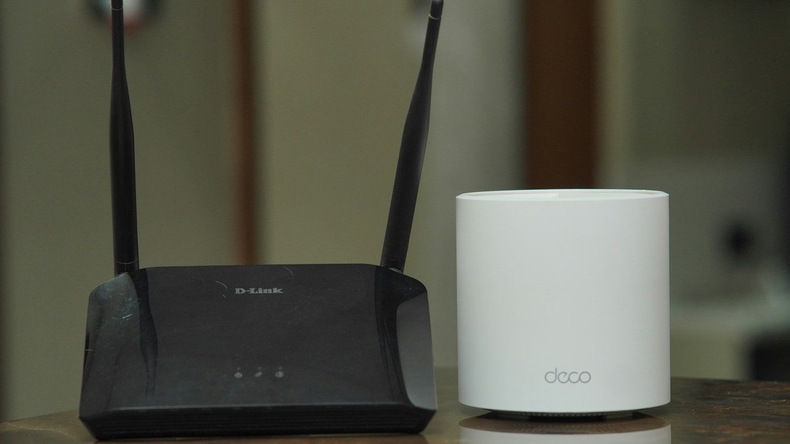 A black broadband router with two aerials next to a white mesh Wi-Fi unit on a table
